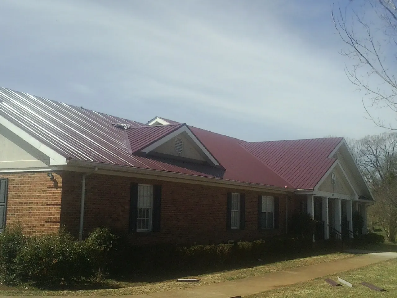 Red metal roof with gabled entries on a long brick building, from a Hail Damage Roof Repair job in Butler
